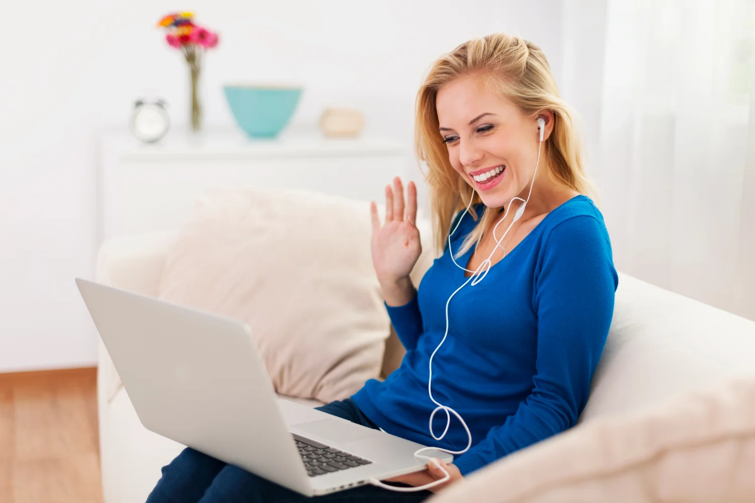 Mujer joven sonriendo y saludando a su laptop con gesto de hola a su terapeuta online
